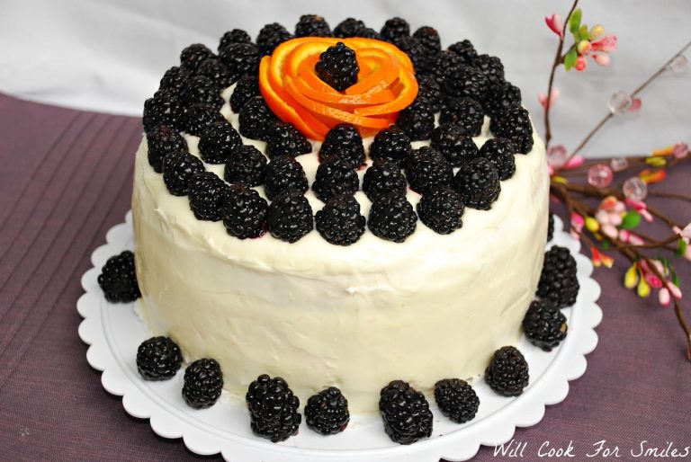 whole blackberry daiquiry cake sitting on a table covered in a purple cloth and decortive branches in the background to the right.