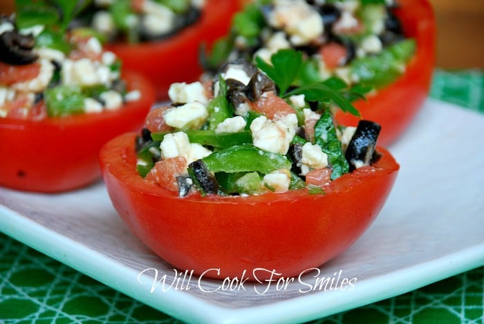 4 stuffed tomato cups on a white rectangular plate on green cloth