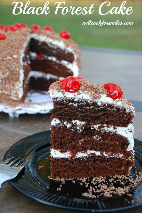 slice of chocoalte case with white frosting and cherries on top on a black plate