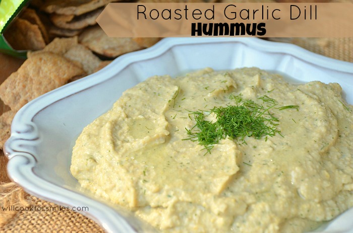 mound of roasted garlic dill hummus in white bowl with bag of chips to back left close up