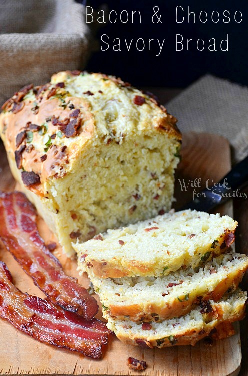 sliced bacon cheese savory bread on a wood cutting board with 2 slices of bacon to the left