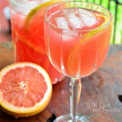 shot from front and slightly above 1 glass of grapfruit sangria with a cut grapefruit below to left and a full pitcher of sangria in background to the left