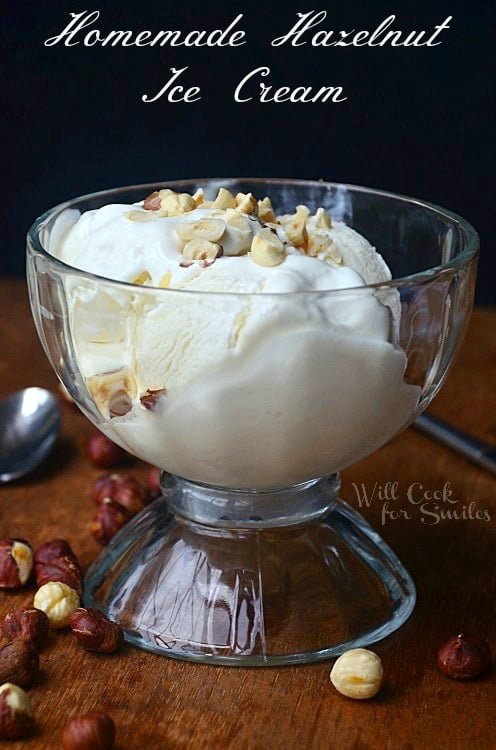 shot from front clear glass bowl of hazelnut ice cream and spoon to bottom left and bottle of creamer to background back left