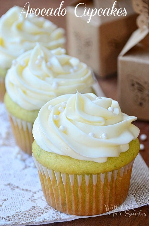 3 avocado cupcakes lined up on decorative cloth on wooden table