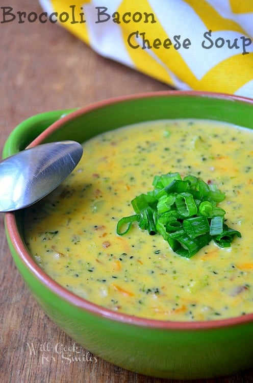 broccoli soup in a green bowl with green onions sliced on top and a spoon to the left 