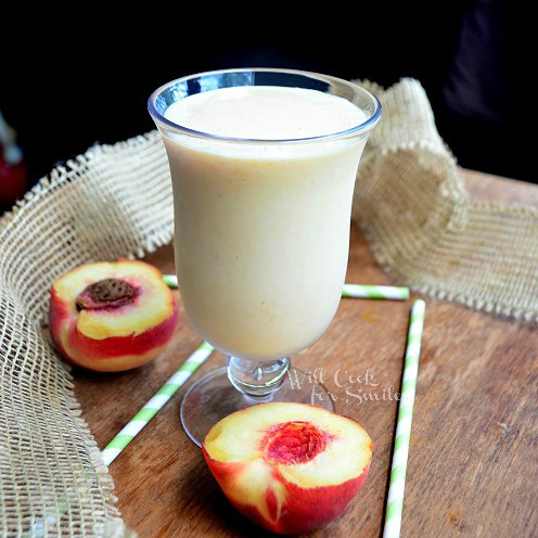 peaches and cream milkshake in a glass with peaches around it and green and white straws 