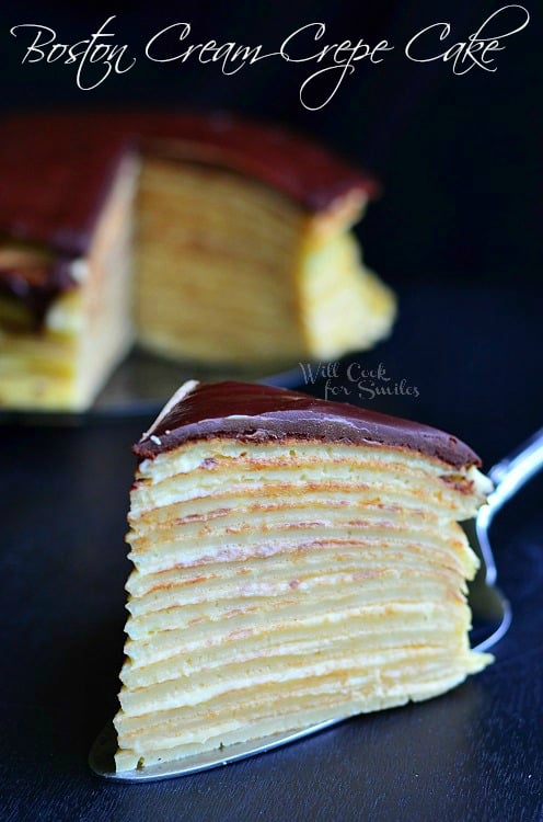 One piece of Boston Cream Crepe Cake sitting on a serving spatula. This cake a layered cake. The crepes make for tiny layers. In-between the layers is a custard. On top of the cake is a chocolate ganache. The rest of the cake fades in the background.