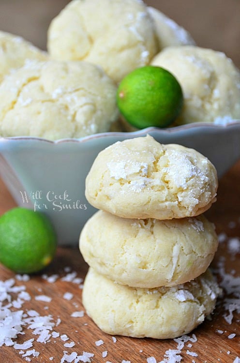 key lime cookies stacked up on a wood table with coconut shavings around 