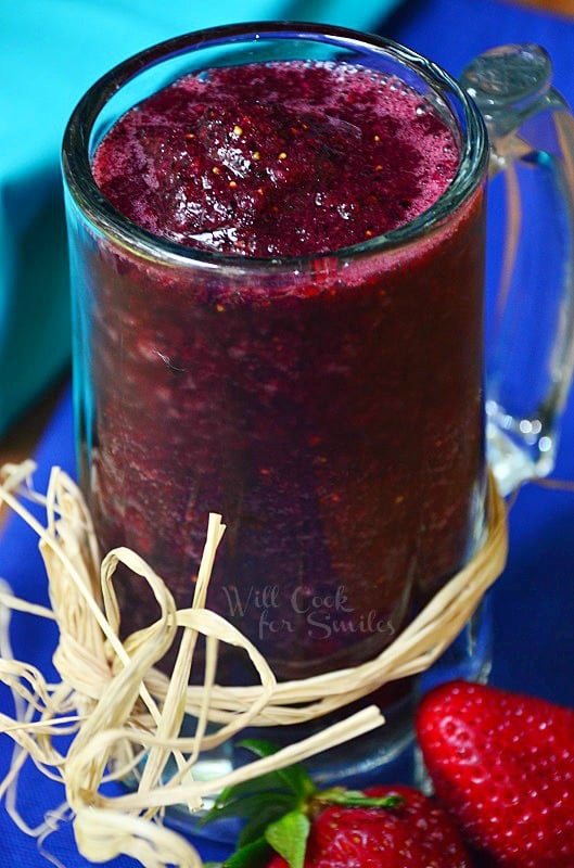 Pomegranate smoothie in a glass much with twine wrapped around the bottom of the outside of the mug with strawberries to the left 