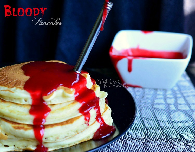 Pancakes on a black plate with strawberry syrup and a fork in them 