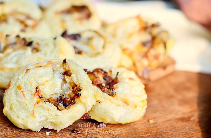 horizonal photo of Caramelized Onion Cheesy Pinwheels on a wood cutting board 