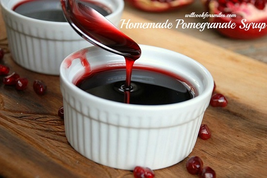 Pomegranate syrup in a bowl with a spoon pouring some in on a wood cutting board 