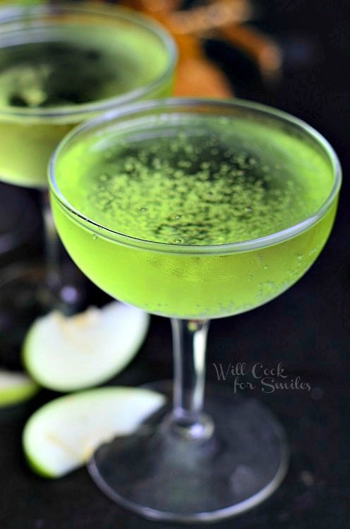 green Sour Apple Champagne cocktail in a wine glass with green apples slices around the bottom 