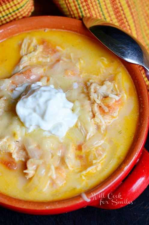 Creamy Chicken Enchilada Soup with a dollop of sour cream on the top in a red bowl with a spoon on the right 