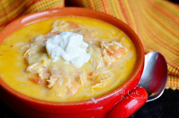 Creamy Chicken Enchilada Soup with a dollop of sour cream on top in a red bowl with a spoon to the right 