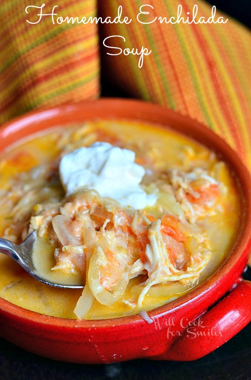 Homemade Enchilada Soup in a red bowl with sour cream on top and a spoon lifting a bite out 