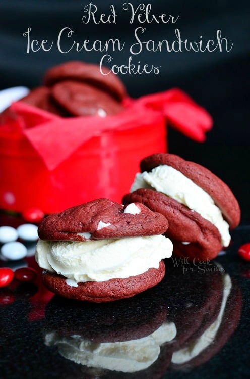 close up view of red velvet ice cream sandwich cookies on a black table with red and white candies scattered around cookies and red and white gift box in background