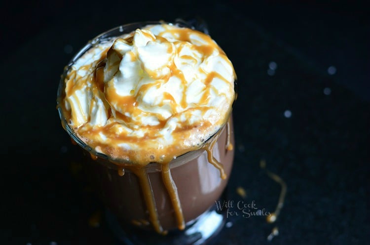 view from above of glass coffee mug filled with skinny salted caramel hot chocolate on a black table. Hot chocolate is topped whipped cream and caramel drizzle running down the side of the glass