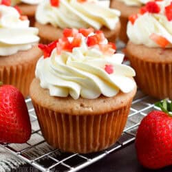 one strawberry cupcakes with white mascarpone frosting and some strawberries.