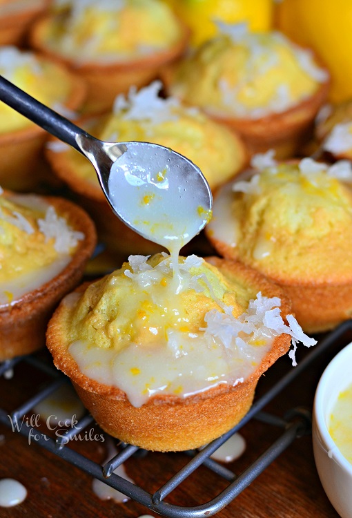 coconut lemon pound cake muffins on cooling rack on wood table as a spoon drizzles coconut syrup over first muffin in foreground