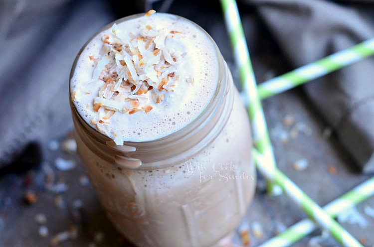 close up view of mason jar filled with coconut mocha milkshake on a grey table with green and white straws scattered around jar and a greyish cloth in background