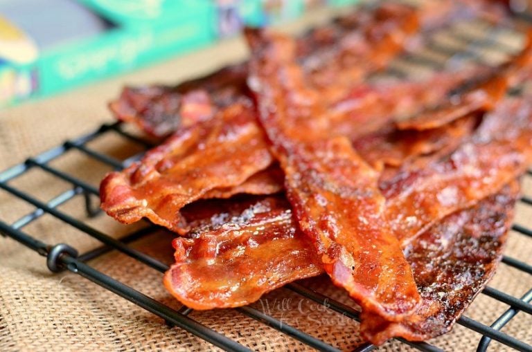 close up view of cooked bacon stacked on a cooling rack with a recipe book in background to the left