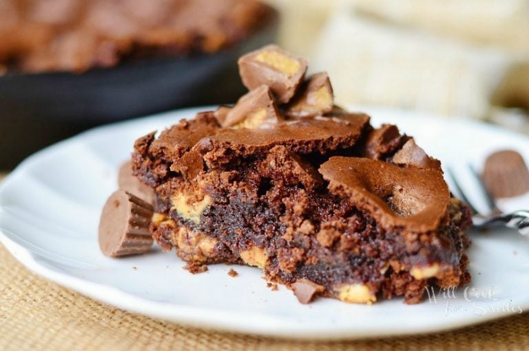 1 portion of ultimate peanut butter cup brownie on a small white plate on brown placemat with whole brownie dish in background to the left