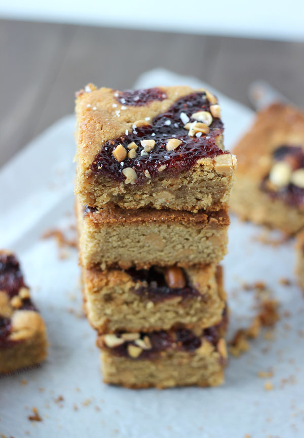 4 salted peanut butter and jelly blondies stacked on a white paper towel on wood table with more blondies below