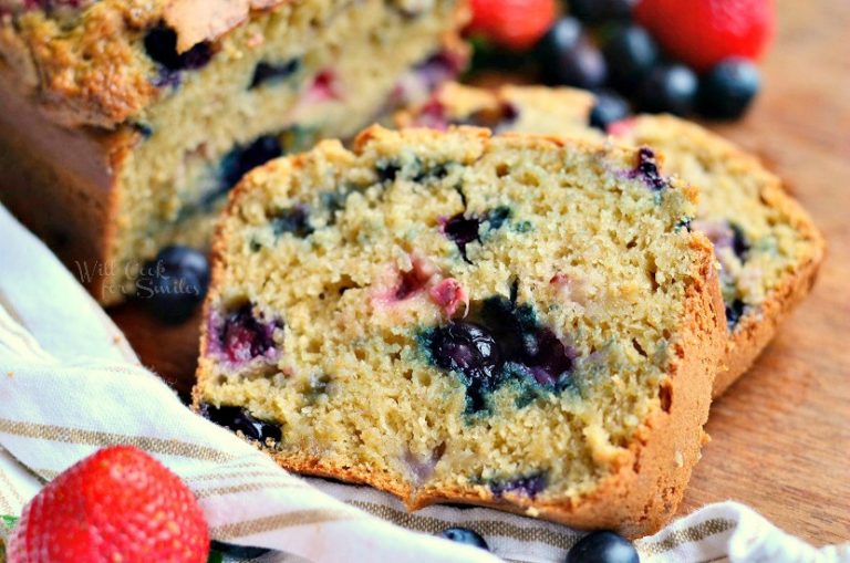 Berry Bread sliced on a wood table with strawberries and blueberries