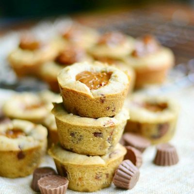 3 dulce de leche peanut butter cup cookies stacked on a brown cloth with mini peanut butter cups at bottom of stack with additional cookies in background