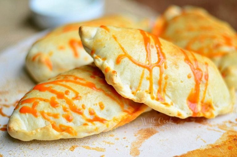 4 homemade buffalo chicken calzoneson a white plate with buffalo sauce drizzled across top