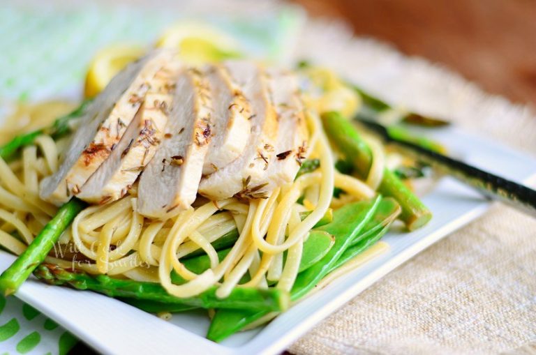 lemon herb pasta on a square white plate with lemon garnish on a brown cloth on top of wood table