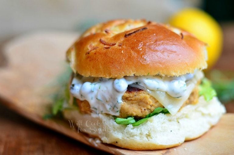 Salmon burger on a bun on wood plank with white sauce on patty with a lemon in the background