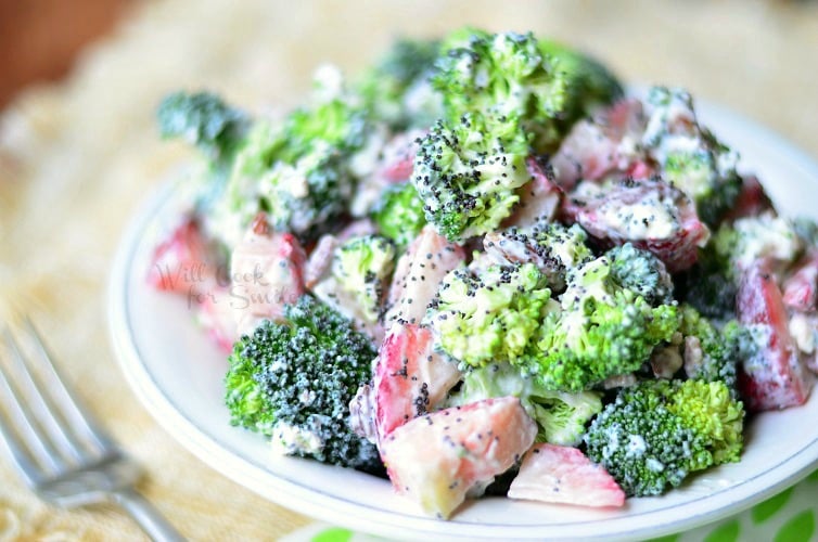 close up view of white bowl filled with strawberry broccoli salad on a white and green cloth with fork to the left