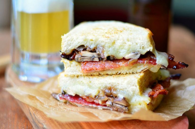 cut and stacked bourbon bacon mushroom abd onion grilled cheese on a brown wax paper wrapper on wood cutting board with a glass beer mug in the background filled halfway with beer