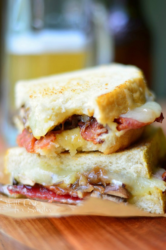 Bourbon Bacon Mushrooms & Onion Grilled Cheese cut in half on a piece of wax paper on a wood cutting board 