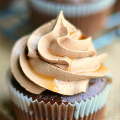 1 bourbon cupcake in cupcake wrapper on brown placemat on wood table with additional cupcakes in background