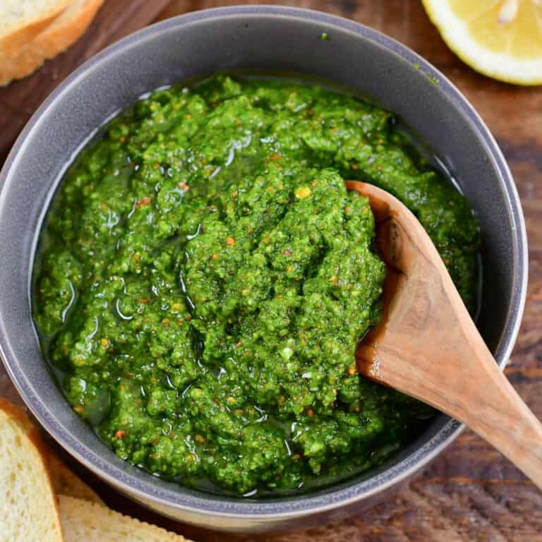 arugula pesto in a grey bowl with a wooden spoon scooping some out.