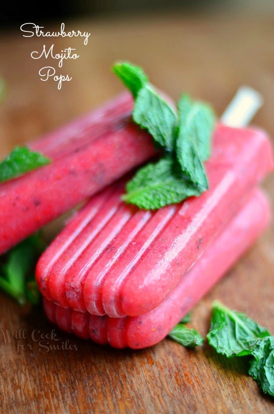 3 strawberry mojito pops on a wooden table with mint leaves dressed across pops