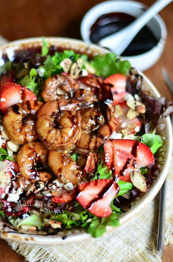 shrimp salad with balsamic reduction dressing on a tan cloth on wood table with small white bowl with more reduction and small spoon in background