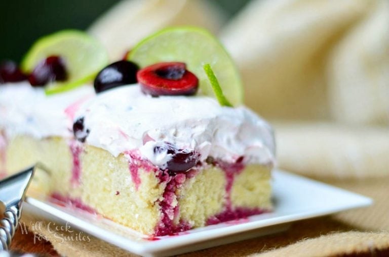 1 slice of cherry limeade poke cake on white rectangular plate in foregroundon a brown placemat with additional slices in background