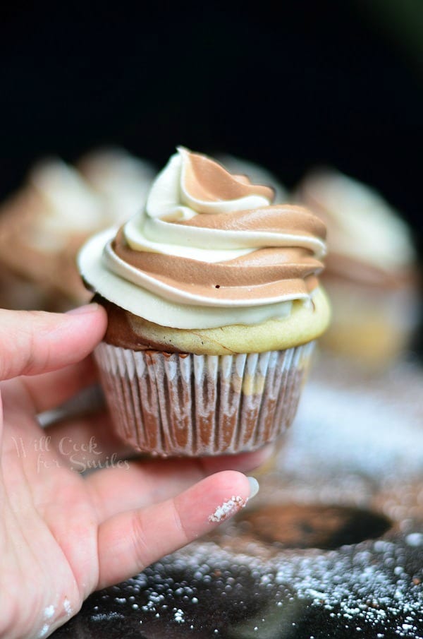 hand holding 1 marble cupcake with marble cream cheese frosting with additional cupcakes in background