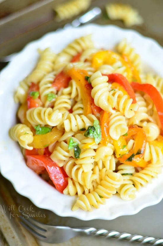 View from above of Roasted Bell Pepper and Garlic pasta salad in a white decorative bowl on a metal baking tray with a fancy fork in front of bowl