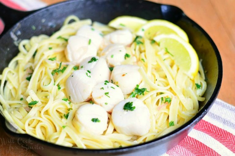 Scallop scampi in a black iron skillet on a red and white cloth with lemon garnish