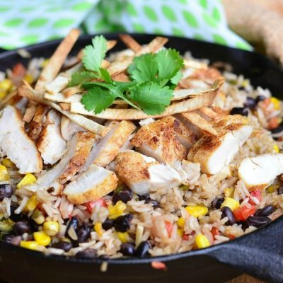 view from above of black skillet with chicken tortilla rice dish on a wood table with green and white cloth in the background