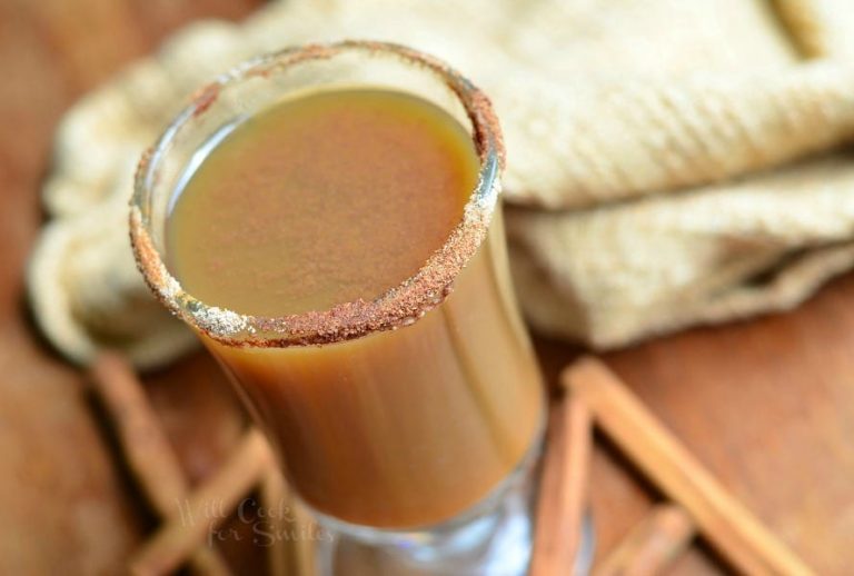 close up view from above of dessert coffee mug filled with light spiced pimpkin after dinner coffee on a wood table with cinnamon sprigs and a brown cloth around the base of glass