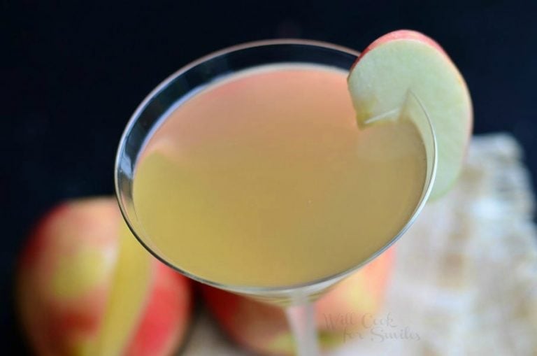 close up view from the top down of a martini glass with apple cider martini on a tan tablecoth and apples below the glass itself.