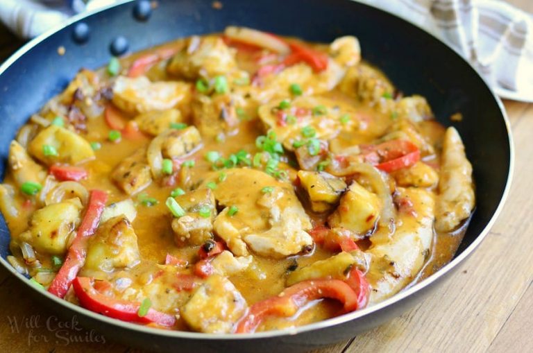 close up view of saute pan with easy thei coconut curry chicken and vegetables on a wood table with tan striped cloth in background behind pan