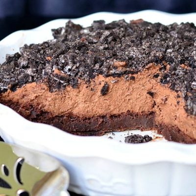 close up view of white baking dish with brownie bottom chocolate mousse pie on a black table with a silver cake cutter in foreground