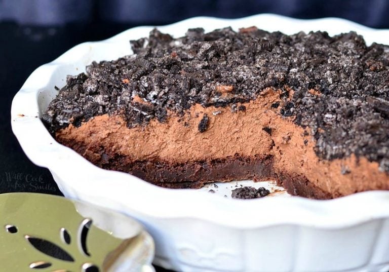 close up view of white baking dish with brownie bottom chocolate mousse pie on a black table with a silver cake cutter in foreground